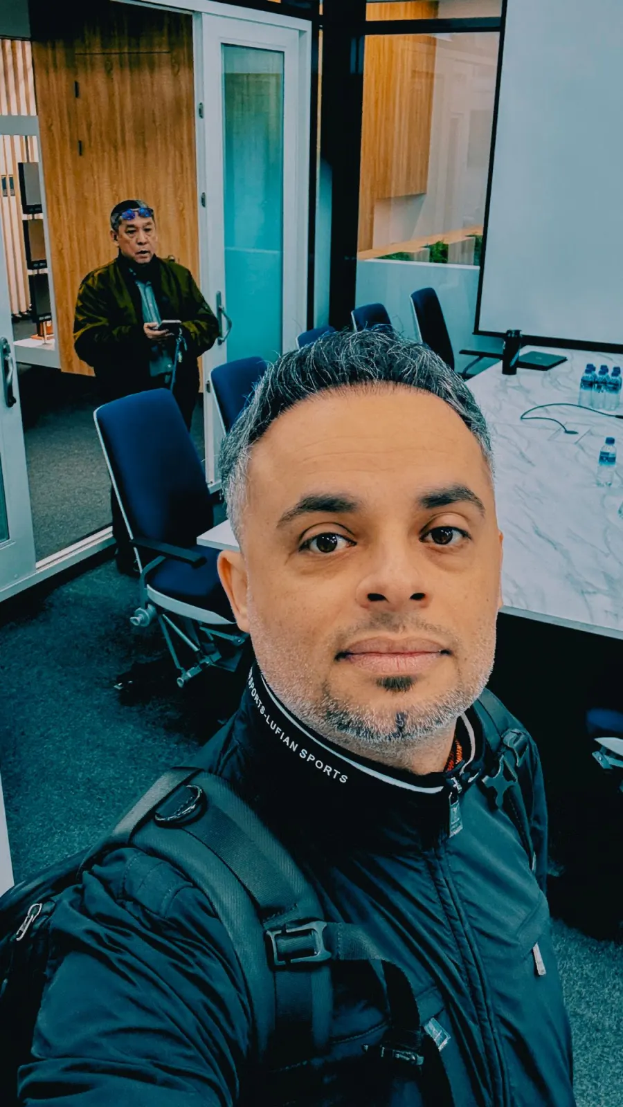 A selfie in a meeting room with a marble table, blue chairs and a projector screen