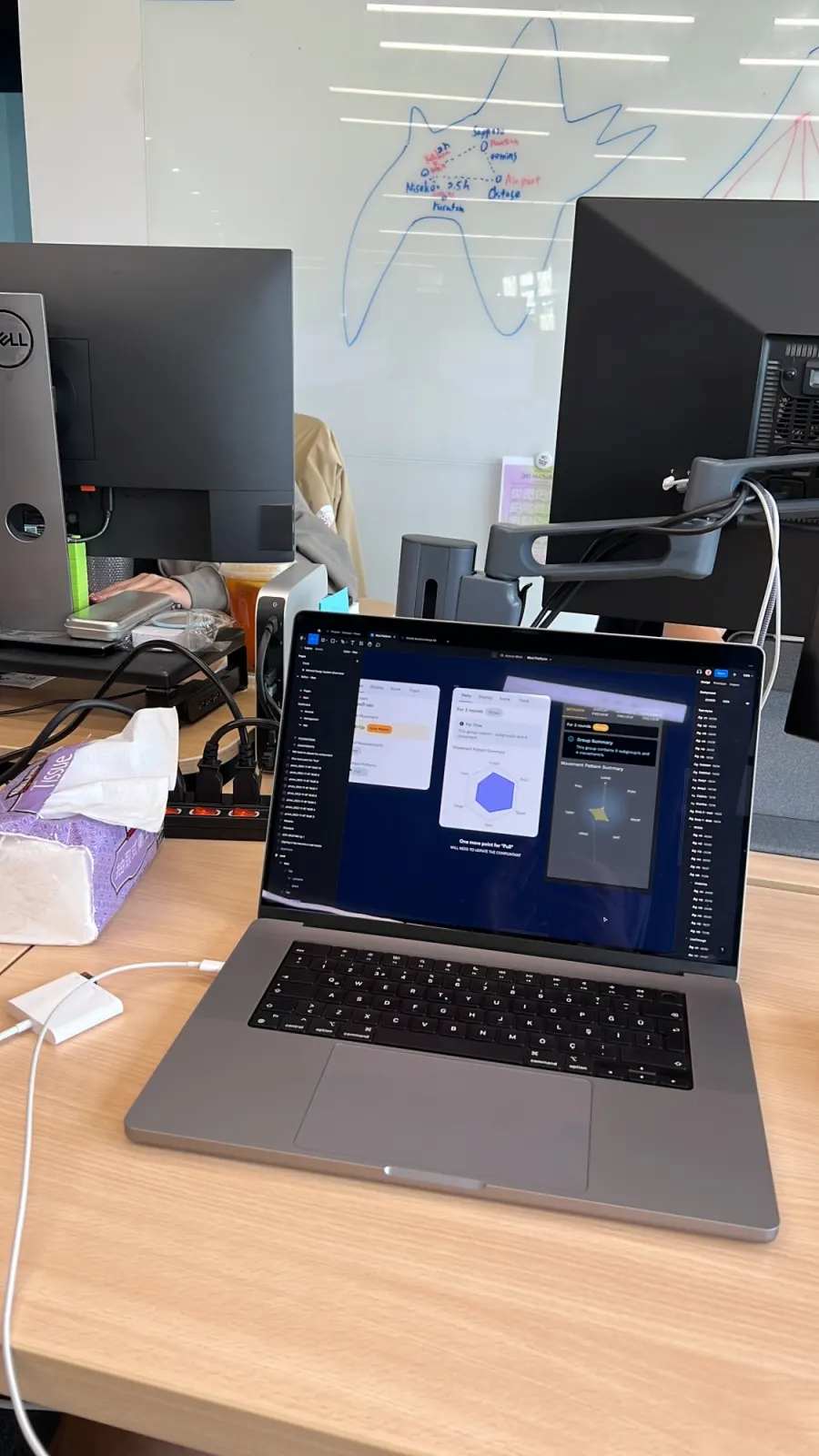 A laptop on a desk showing the WOD.co platform in Figma, with monitors and a whiteboard map behind it